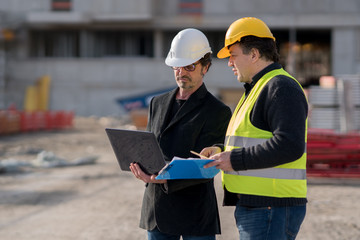 Fototapeta premium Civil engineer giving instructions to a construction worker using a computer laptop. Outdoors