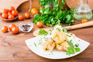 Appetizing ready-to-eat cabbage rolls with minced meat, sour cream and fresh herbs on a plate on a wooden table