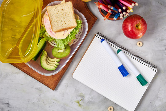Concept of school lunch break with healthy lunch box and school supplies on white desk, selective focus, flat lay