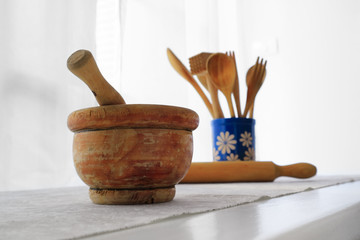 Closeup of old wooden mortar with pestle inside on white table with grey tablecloth. White wall and...