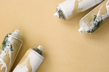 Some used orange aerosol spray cans with paint drips lies on a blanket of soft and furry light orange fleece fabric. Classic fashion design color. Graffiti hooliganism concept