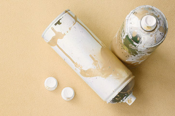 Some used orange aerosol spray cans and nozzles with paint drips lies on a blanket of soft and...