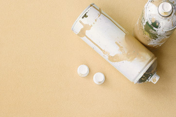 Some used orange aerosol spray cans and nozzles with paint drips lies on a blanket of soft and...