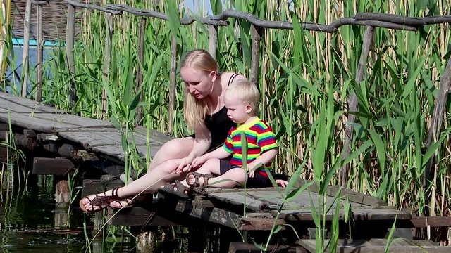 A young mother and son are resting on the bridge by the river. Lifestyle concept