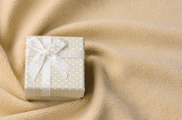 A small gift box in orange with a small bow lies on a blanket of soft and furry light orange fleece...