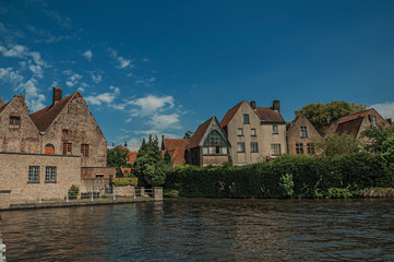 Fototapeta na wymiar Old brick buildings and greenery on the canal's edge in a sunny day at Bruges. With many canals and old buildings, this graceful town is a World Heritage Site of Unesco. Northwestern Belgium.