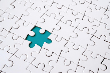 Close-up texture of a white jigsaw puzzle in assembled state with missing elements forming a blue pad for text. Copy space - obrazy, fototapety, plakaty