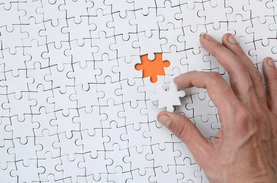 The texture of a white jigsaw puzzle in the assembled state with one missing element that the male hand puts in