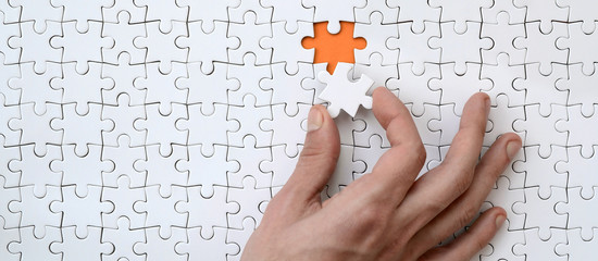 The texture of a white jigsaw puzzle in the assembled state with one missing element that the male hand puts in