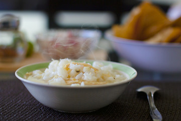 Pozole blanco con pollo, servido en un plato hondo contemporaneo, acompañado de  chile de arbol, limones, rabanos y tostadas