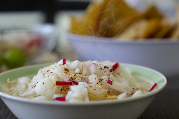 Pozole blanco con pollo, servido en un plato hondo contemporaneo, acompañado de  chile de arbol, limones, rabanos y tostadas