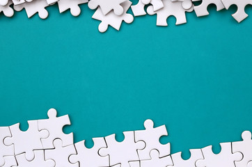 Fragment of a folded white jigsaw puzzle and a pile of uncombed puzzle elements against the background of a blue surface. Texture photo with space for text - obrazy, fototapety, plakaty