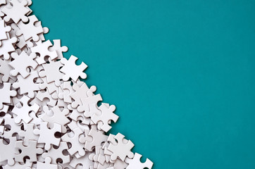 A pile of uncombed elements of a white jigsaw puzzle lies on the background of a blue surface....