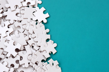 A pile of uncombed elements of a white jigsaw puzzle lies on the background of a blue surface. Texture photo with copy space for text - obrazy, fototapety, plakaty