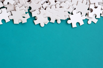 A pile of uncombed elements of a white jigsaw puzzle lies on the background of a blue surface....