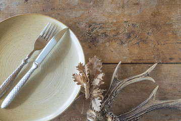 Table setting for hunter's dinner: vintage cutlery on rustic plate, dry oak leaf on old wooden...