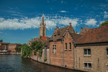 Steeple and old brick buildings on the canal's edge in a sunny day at Bruges. With many canals and old buildings, this graceful town is a World Heritage Site of Unesco. Northwestern Belgium.