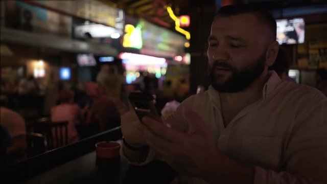 Man sitting in pub at the evening and browsing internet on smartphone

