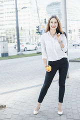 Girl in a business suit on the streets of the city with an apple. A young woman speaks through a mobile phone. The lady smiles.