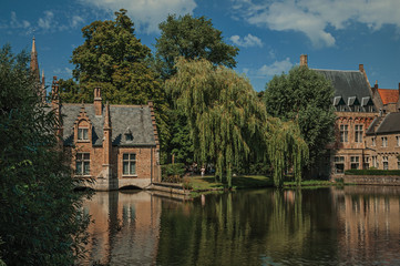 Fototapeta na wymiar Amazing lake surrounded by greenery and old brick building on the other side in Bruges. With many canals and old buildings, this graceful town is a World Heritage Site of Unesco. Northwestern Belgium.