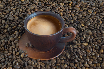 Cup of hot coffee against the background of fried coffee beans close up.