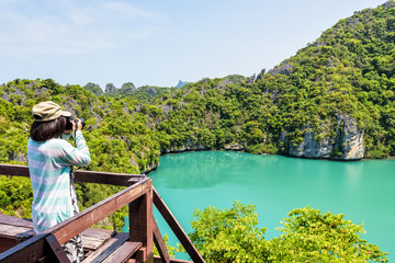 Fototapeta premium Woman tourist on Koh Mae Ko island viewpoint use camera taking photos at beautiful nature landscape of Thale Nai or Blue Lagoon (Emerald Lake) in Mu Ko Ang Thong National Park, Surat Thani, Thailand