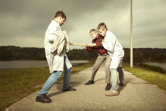 Two older retro paramedic freak hunters in medical coats fighting with crazy man in park