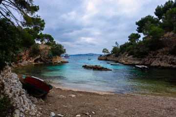 Seascape with colorful waters in small mediterranean bay with boat in the foreground and dramatic sky.