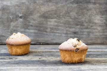 Two muffins with raisins sprinkled with powdered sugar on a wooden background