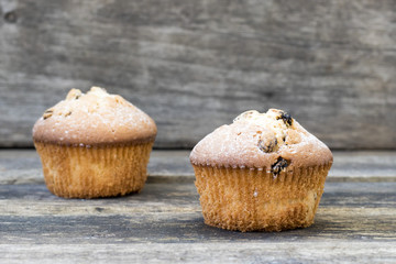 Two muffins with raisins sprinkled with powdered sugar on a wooden background