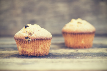 Two muffins with raisins sprinkled with powdered sugar on a wooden background