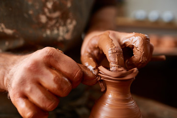 Close-up hands of a male potter in apron molds bowl from clay, selective focus