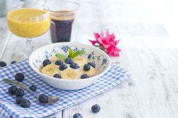 Delicious and healthy breakfast. Oatmeal with berries, aromatic coffee and fresh orange juice. White wooden background and blue napkin. Copy space. 