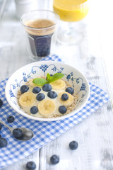 Delicious and healthy breakfast. Oatmeal with berries, aromatic coffee and fresh orange juice. White wooden background and blue napkin. Good morning