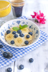 Delicious and healthy breakfast. Oatmeal with berries, aromatic coffee and fresh orange juice. White wooden background and blue napkin. Pink flowers
