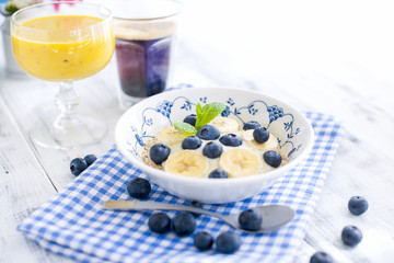 Delicious and healthy breakfast. Oatmeal with berries, aromatic coffee and fresh orange juice. White wooden background and blue napkin. Copy space. 