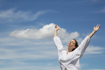 Young woman in white shirt with raised hands and fluffy sky background