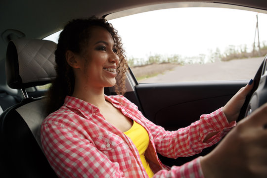 Young beautiful smiling woman driving a car. Her cute daughter sitting on rear and enjoying.