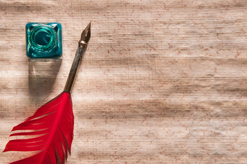 Red quill pen and black inkwell on a papyrus leaf