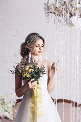 beautiful girl in wedding dress is standing near crystal curtains and holding bouquet.