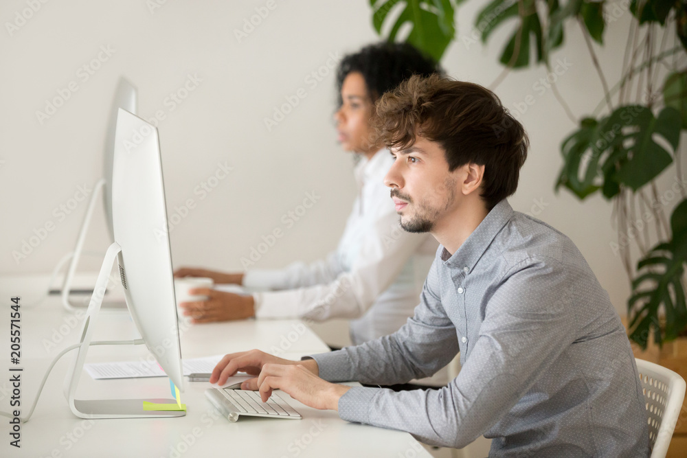 Wall mural young employee focused on computer in multiracial shared office, serious guy programmer or web desig