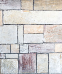 Detail einer Mauer aus viereckigen, pastellfarbenen Steinen in unterschiedlicher Größe 