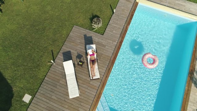 AERIAL, POV: Relaxed woman finds out remote controlled plane is trying to film her sunbathing so she tries to bring it down. Unknown intruder flies his drone and invades girl's privacy as she suntans.