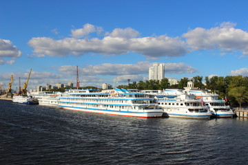 Fototapeta na wymiar Three cruise ships at the pier of the Northern river port in Moscow on the background of port cranes and blue summer sky with clouds