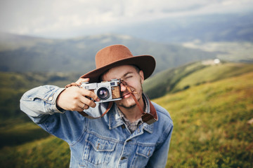 travel and wanderlust. stylish traveler man taking photos on top of mountains with photo camera in clouds. space for text. hipster guy traveling, making images. amazing atmospheric moment.