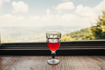 cranberry juice in glass on wooden table with view on mountains and sky. stylish red drink on porch. summer vacation and relax concept. travel and wanderlust. space for text
