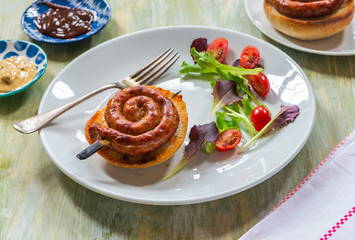 Chilli pork pinwheel sausages on a bun with fresh green leaf lettuce salad