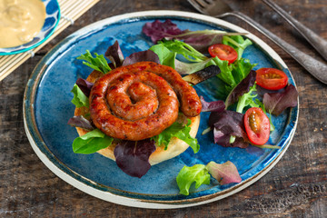 Chilli pork pinwheel sausages on a bun with fresh green leaf lettuce salad