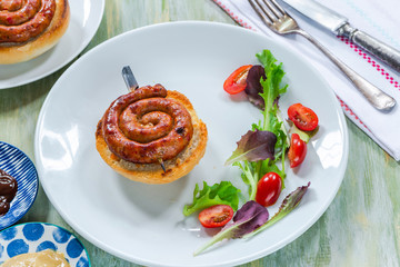 Chilli pork pinwheel sausages on a bun with fresh green leaf lettuce salad