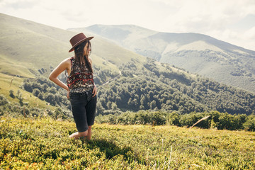 Fototapeta na wymiar travel and wanderlust concept. stylish traveler hipster girl in hat, walking in sunny mountains. summer vacation. space for text. amazing atmospheric moment. woman traveling